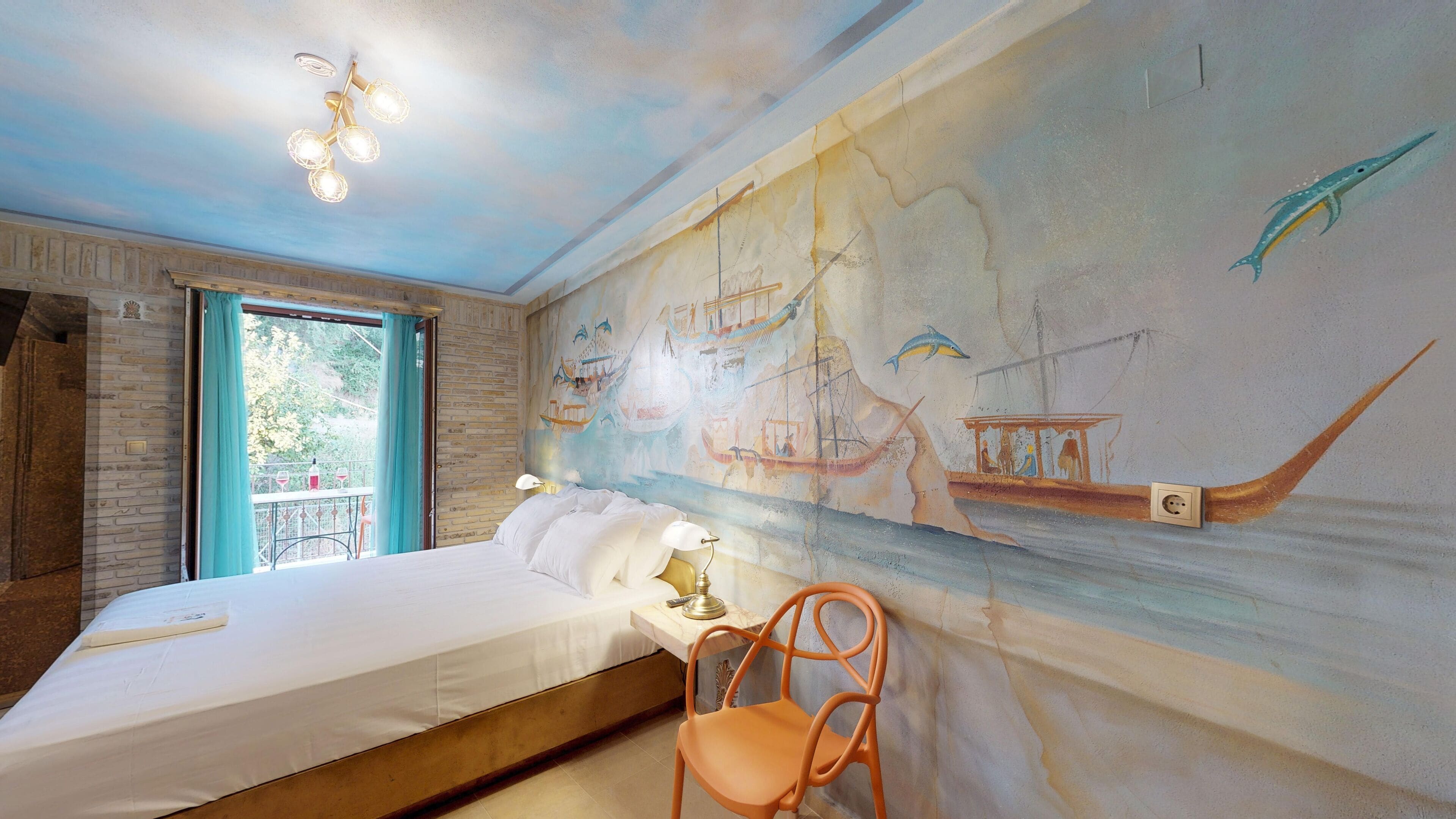 Una habitación con cama, una silla, un mural de barcos y criaturas marinas, y una ventana con cortinas.