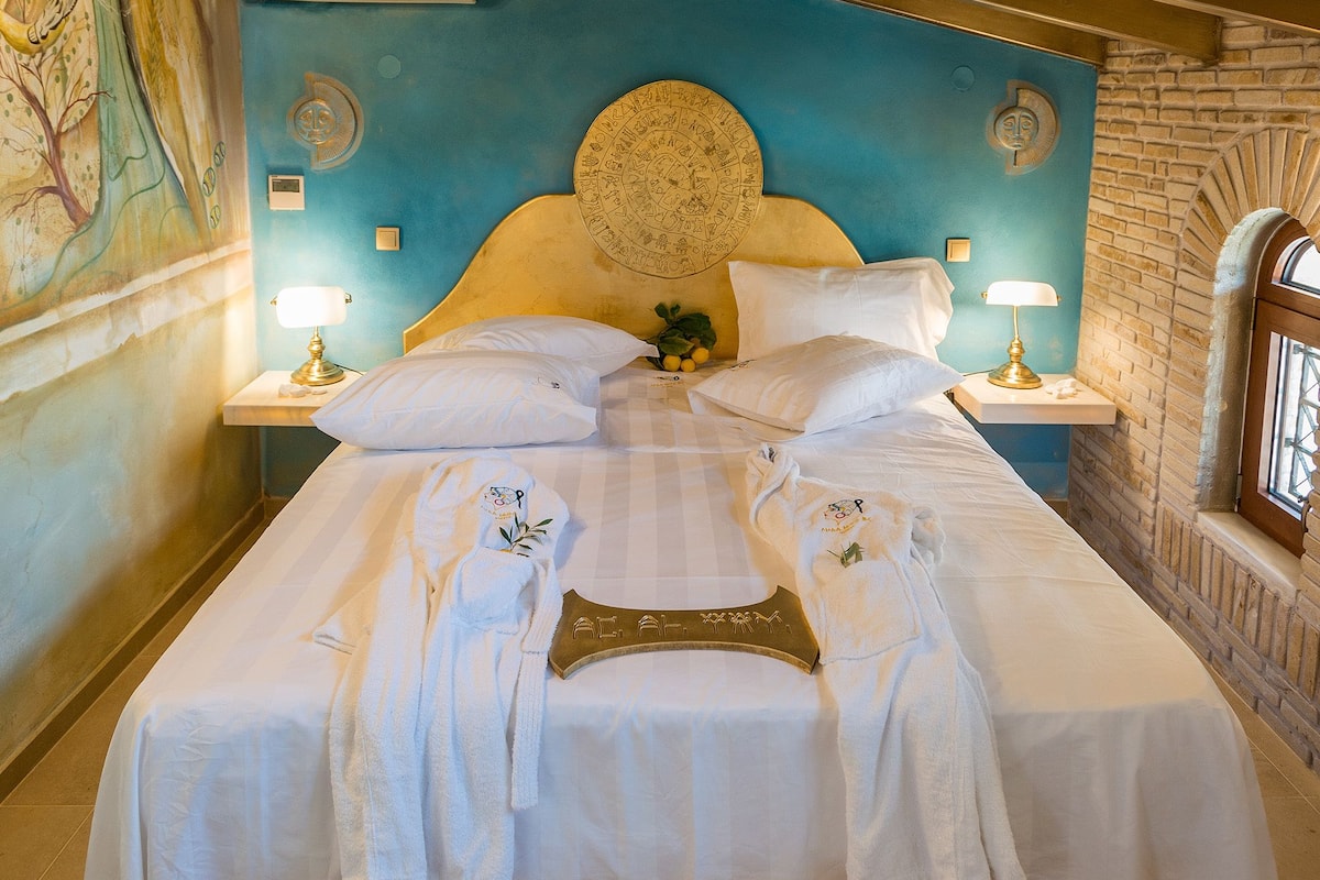 A large bed with white linens, two bedside tables with lamps, a wall mural, and a brick wall with a window.