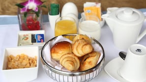 A breakfast table with croissants, orange juice, milk, and a bowl of cereal.