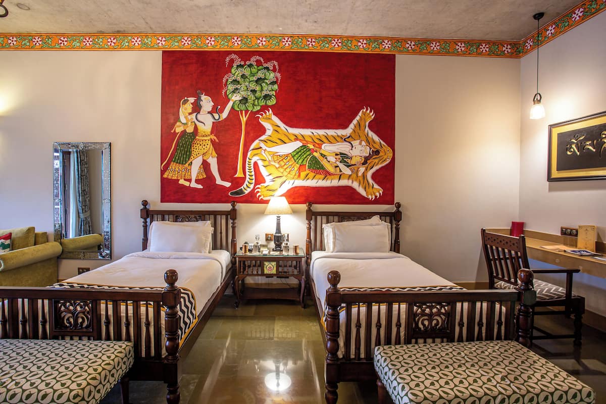 A hotel room with two beds, a mirror, a red tapestry, a wooden table, and a chair.