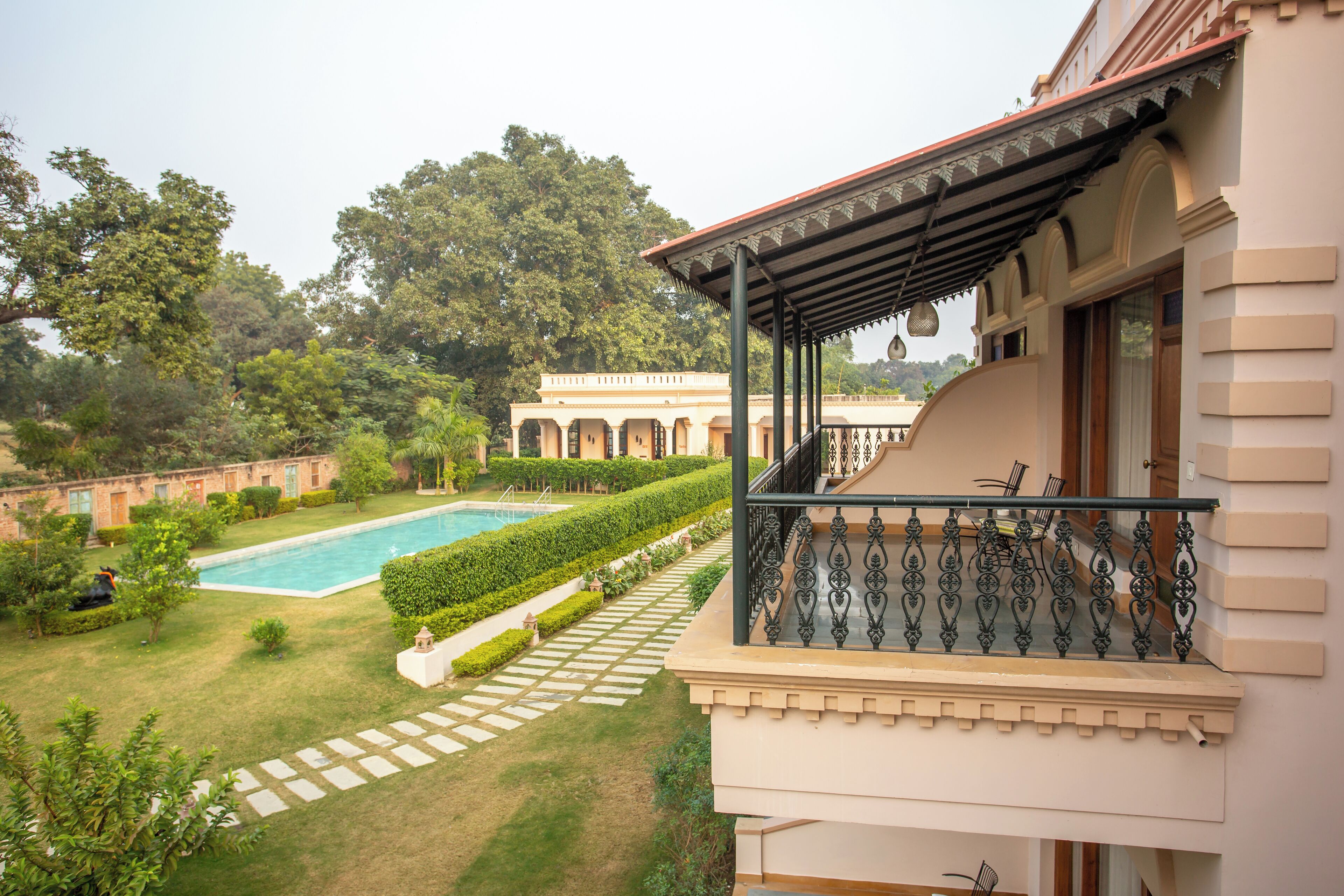 Vista da piscina com um edifício e varanda coberta, piscina e jardim bem cuidado.