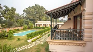 Vista da piscina com um edifício e varanda coberta, piscina e jardim bem cuidado.
