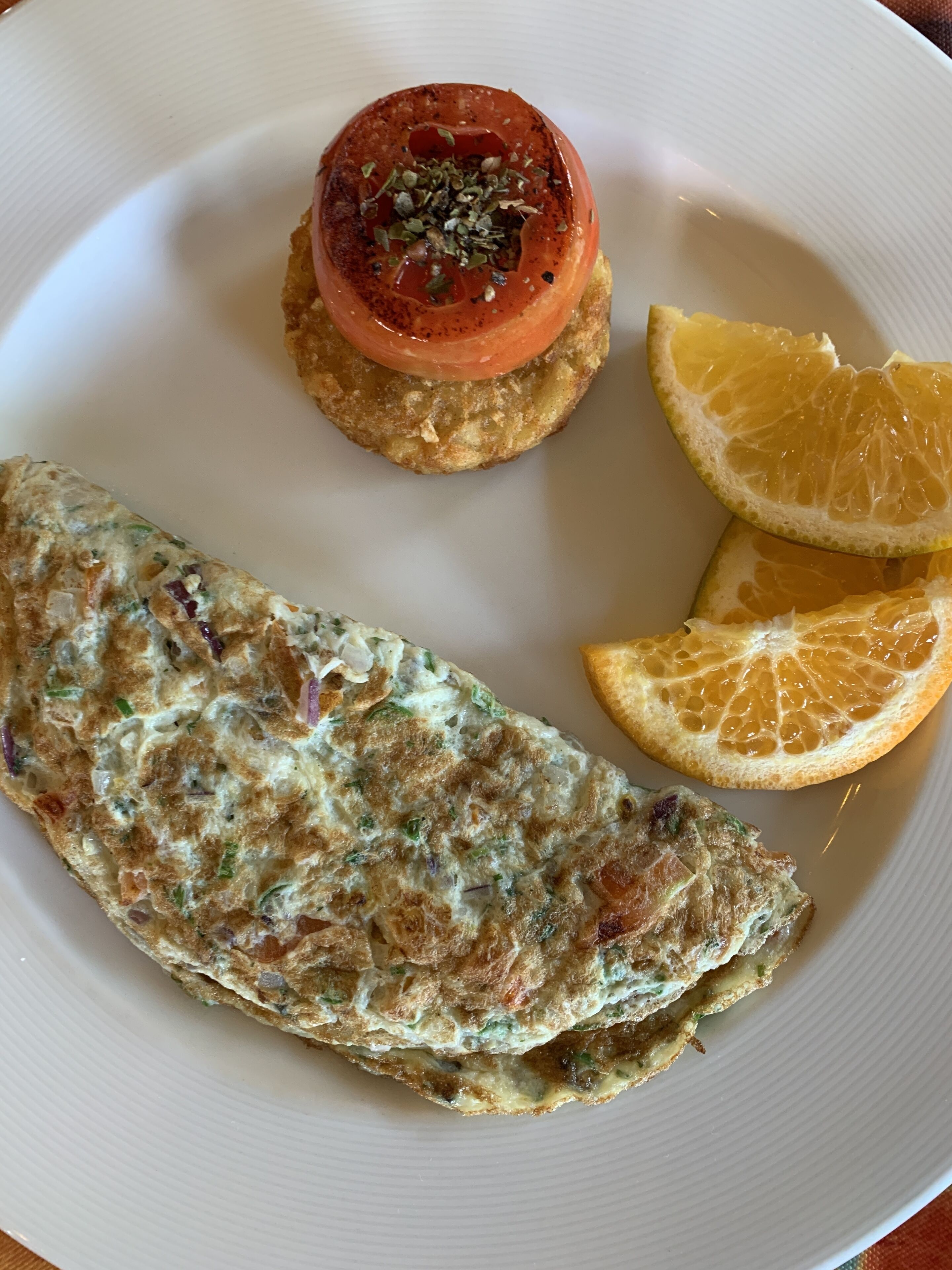 Une assiette avec une part d’omelette, une tomate garnie d’herbes et une tranche d’orange.