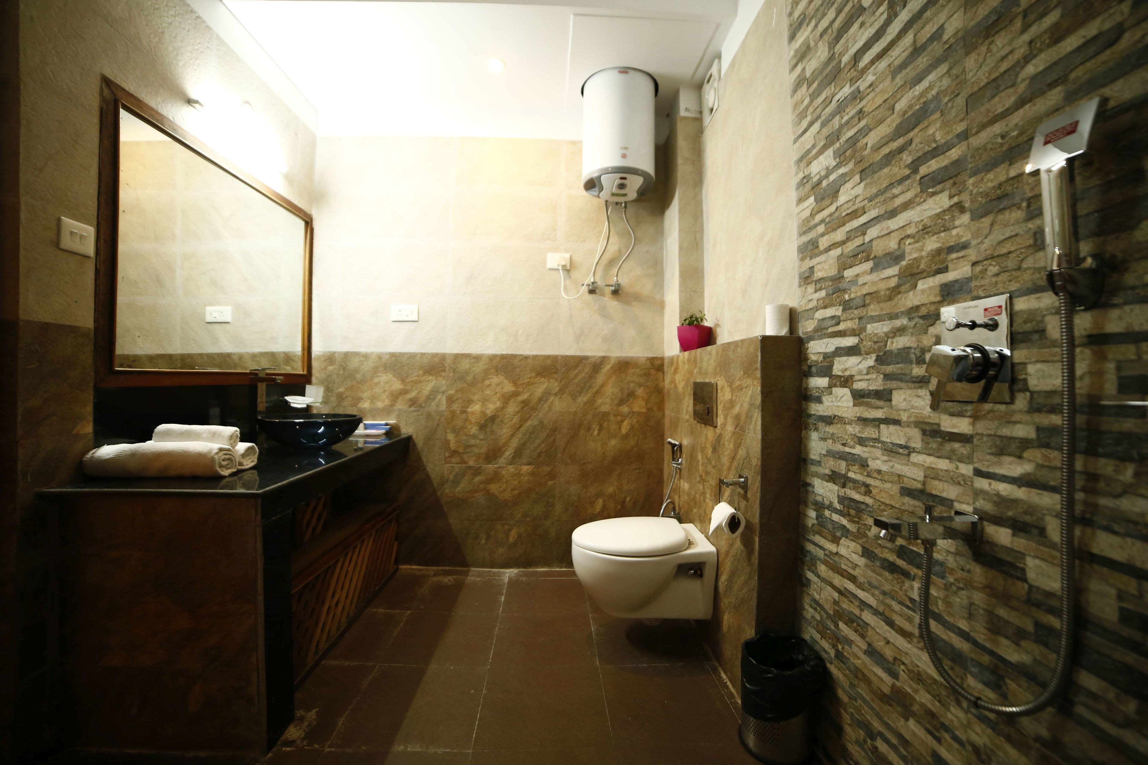 A bathroom with a toilet, a sink, a mirror, a towel rack, a shower, and a water heater.