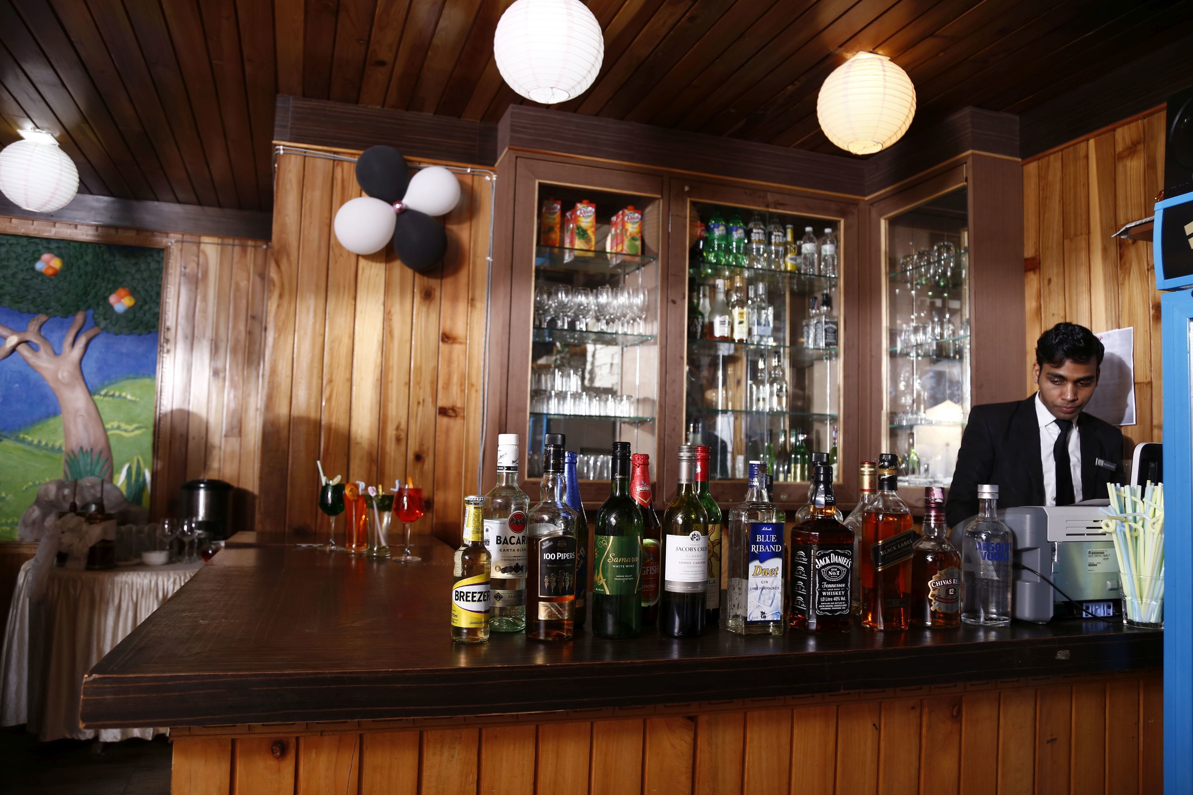 A bar area with wooden paneling, a variety of liquor bottles, and a bartender.