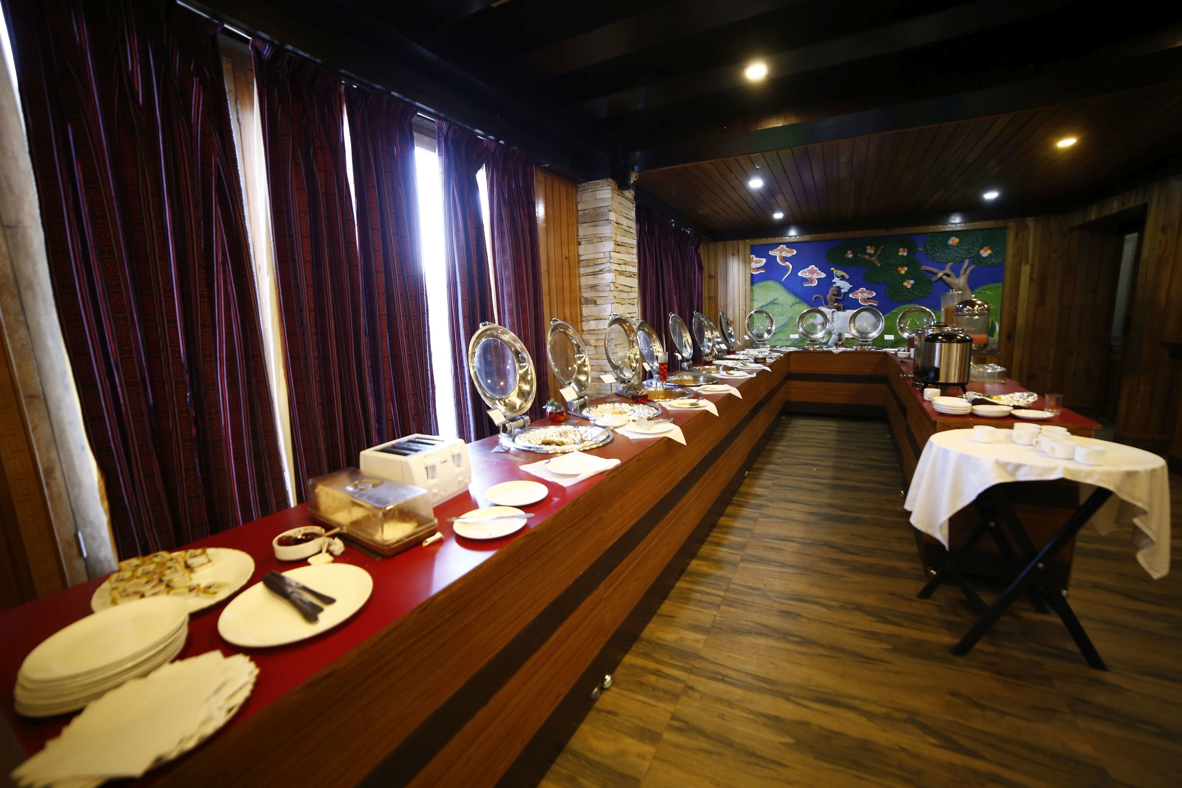 A long dining table with multiple plates and cutlery, set against a backdrop of wooden walls and a mural.