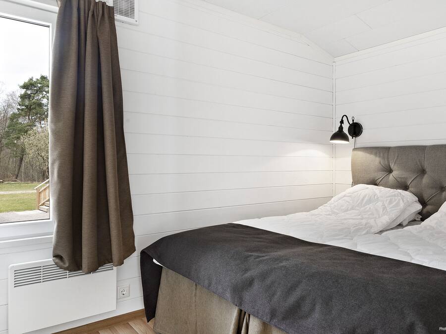 Une chambre à coucher avec un lit, une fenêtre avec des rideaux, une lampe fixée au mur et un radiateur.