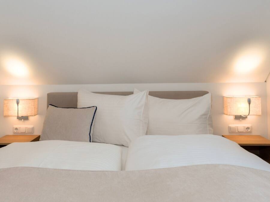A double bed with white linens in a room with two bedside tables, each with a lamp.