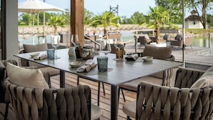Un espace de restauration en plein air avec une table dressée pour quatre personnes, entourée de fauteuils confortables, et offrant une vue sur une piscine et un paysage tropical.
