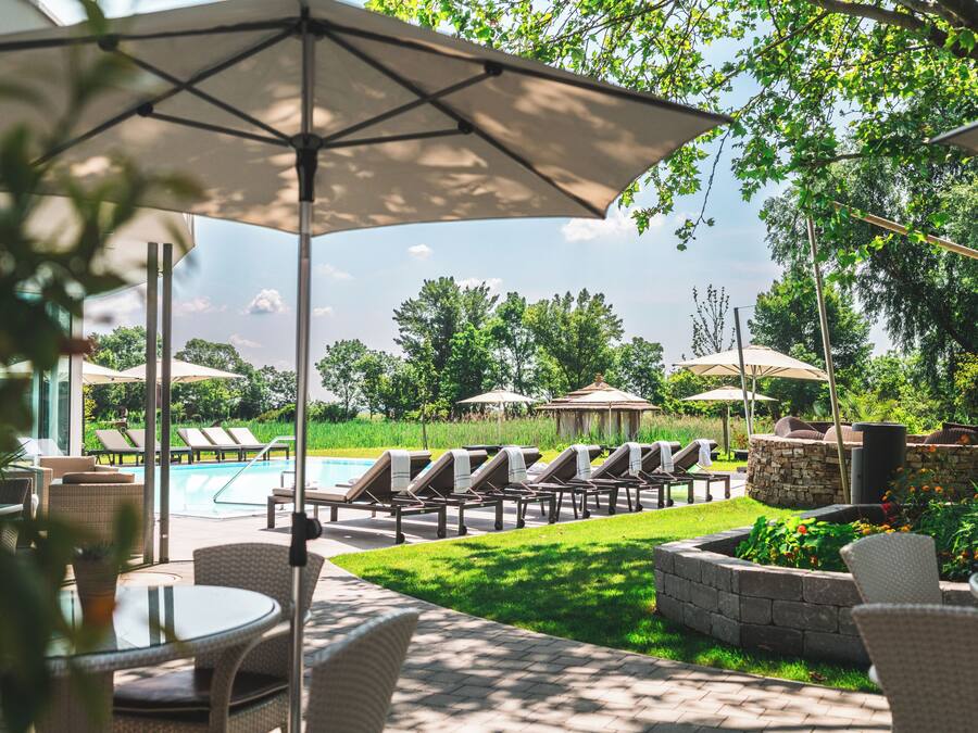 A poolside area with lounge chairs, umbrellas, and a view of the pool and greenery.