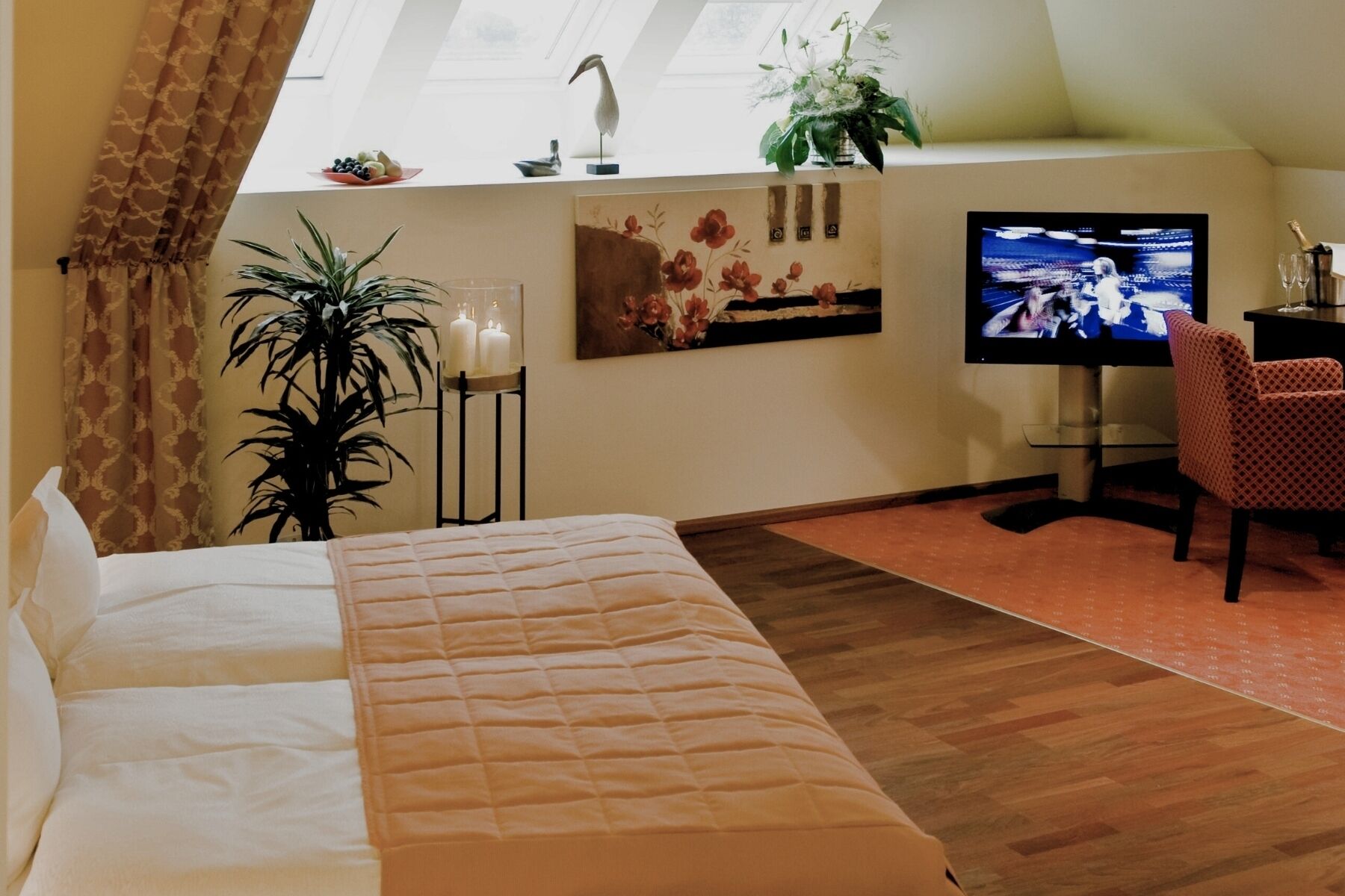 Habitación de hotel con una cama, televisor, escritorio con silla y una planta en maceta.