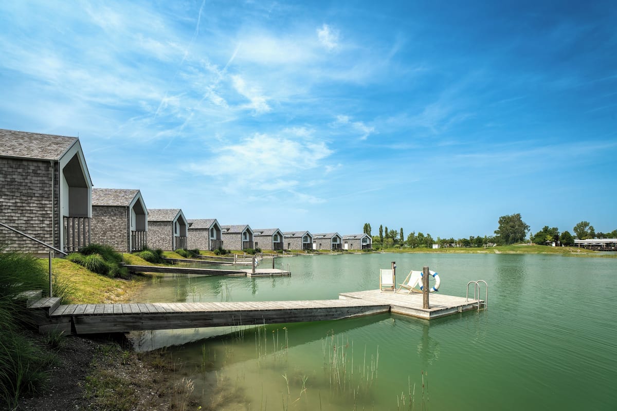 Een hotel aan het meer, met een steiger die in het water uitloopt, omringd door stenen gebouwen met puntige daken.
