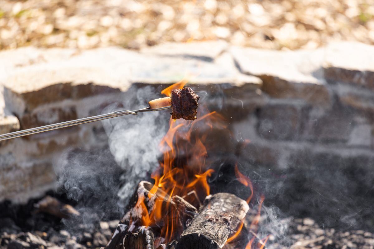 Primer plano de carne asándose sobre fuego abierto.