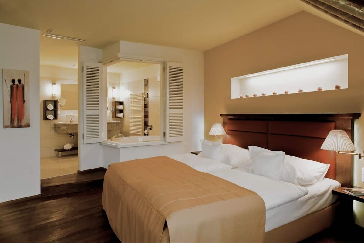 Een hotelkamer met een groot bed, bedlampen, een spiegel en uitzicht op de badkamer.
