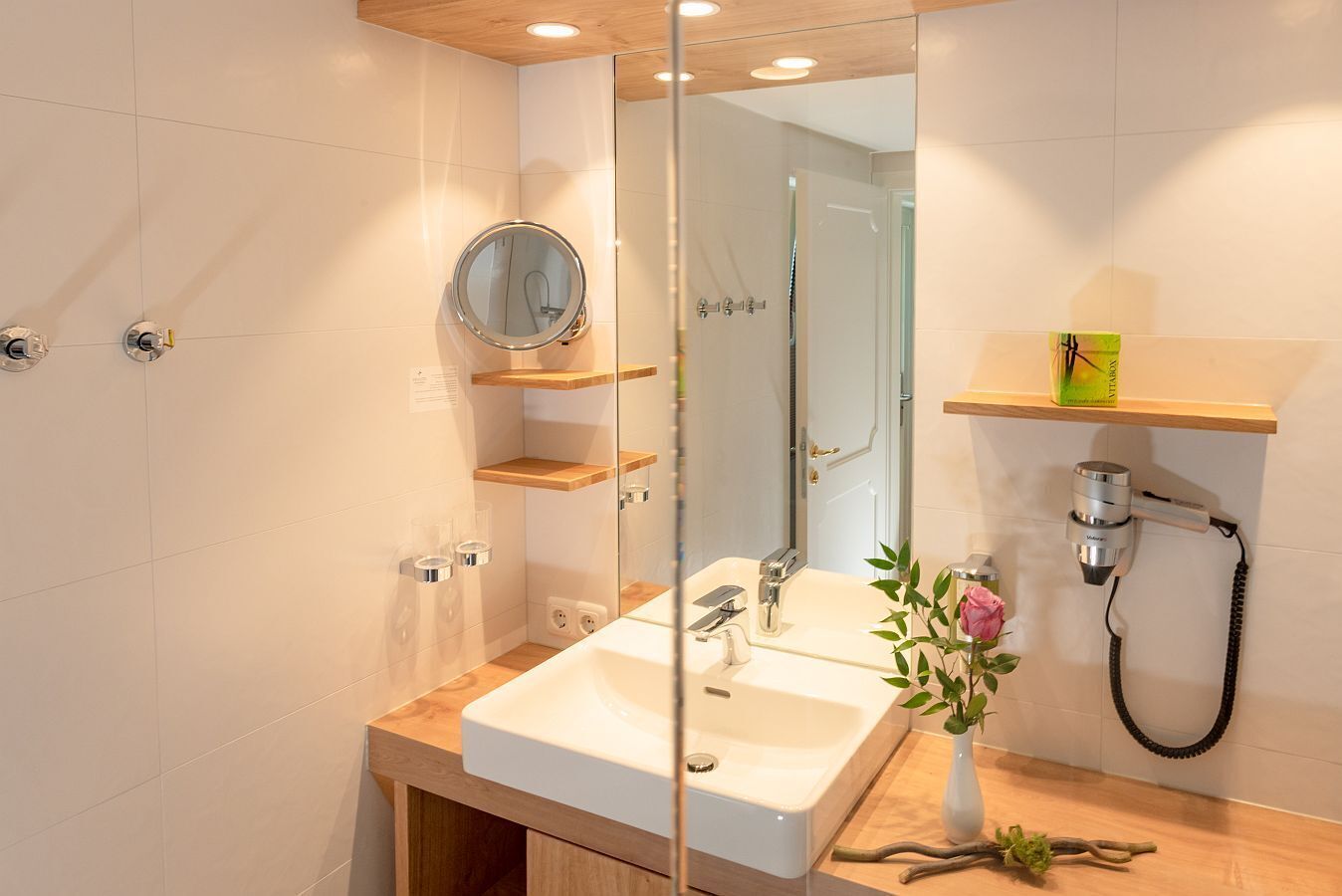 Un baño moderno con un lavamanos blanco, un espejo y un cabezal de ducha de mano.