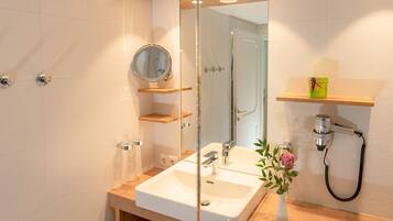 Un baño moderno con un lavamanos blanco, un espejo y un cabezal de ducha de mano.