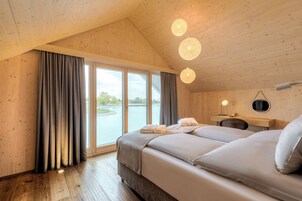 Una habitación de cabaña de madera con una ventana grande, una cama, un escritorio y una lámpara colgante.