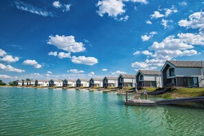 Een rij vakantiehuisjes aan het water, met een steiger die uitsteekt in een rustig meer, onder een helderblauwe hemel.