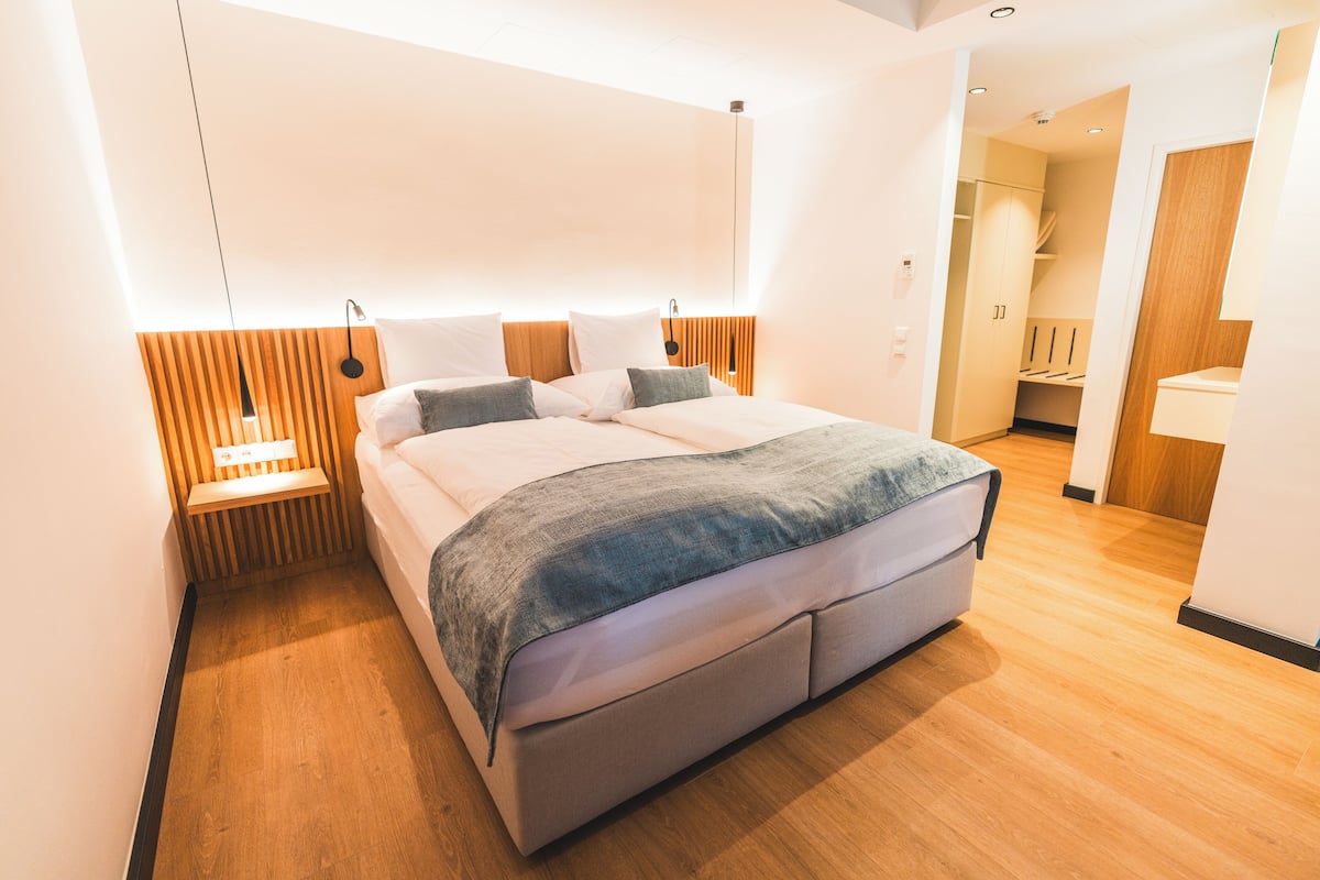 Een moderne slaapkamer met een groot bed, houten hoofdbord, nachtkastjes en een inloopkast.