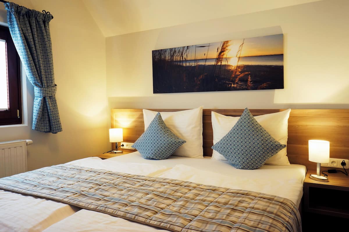 Een net opgemaakt bed met een geruite sprei, twee gestreepte kussens en een hoofdbord met een schilderij erboven.