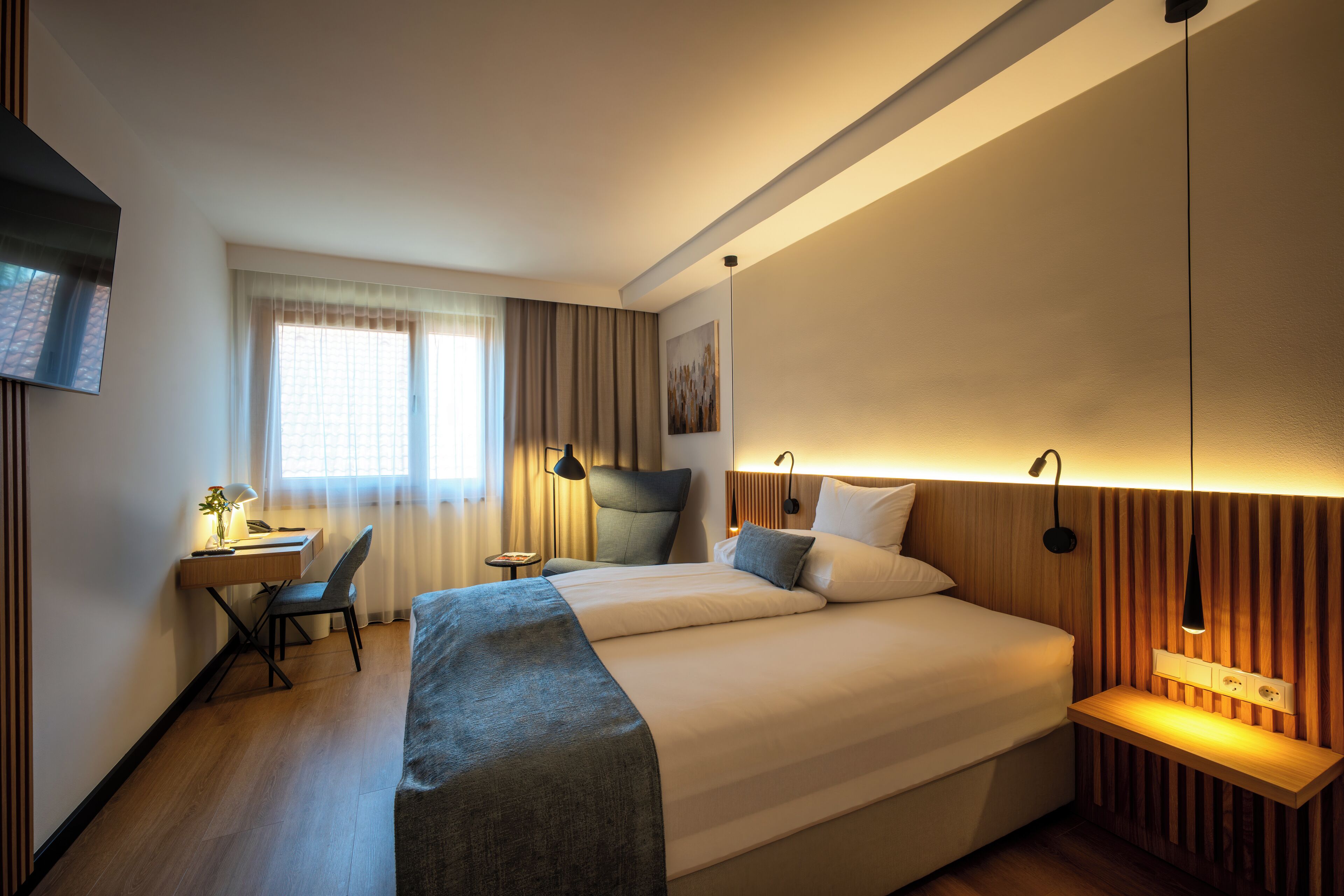 Een hotelkamer met een bed, bureau, stoel en een aan de muur bevestigde televisie.