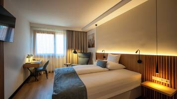 Een hotelkamer met een bed, bureau, stoel en een aan de muur bevestigde televisie.