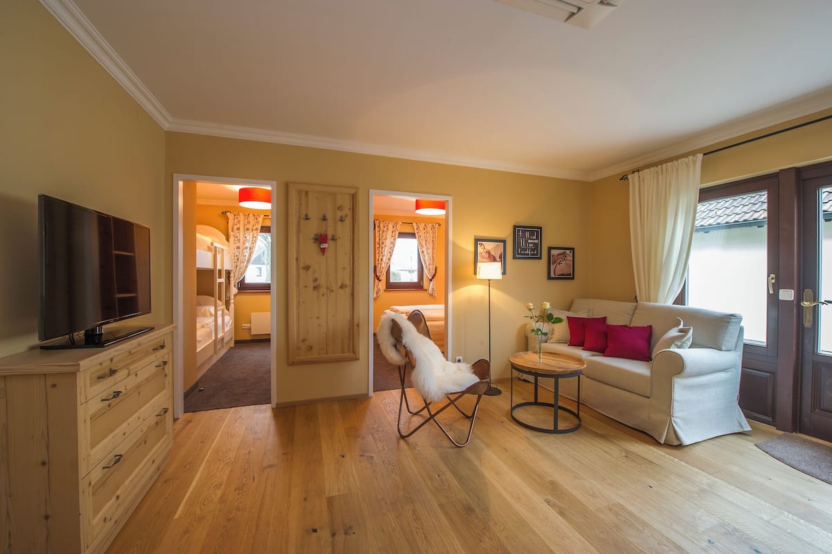 Een woonkamer met een bank, een fauteuil, een televisie en een houten kast.