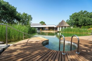 Una terraza de madera que conduce a una piscina, con una estructura de techo de paja al fondo.