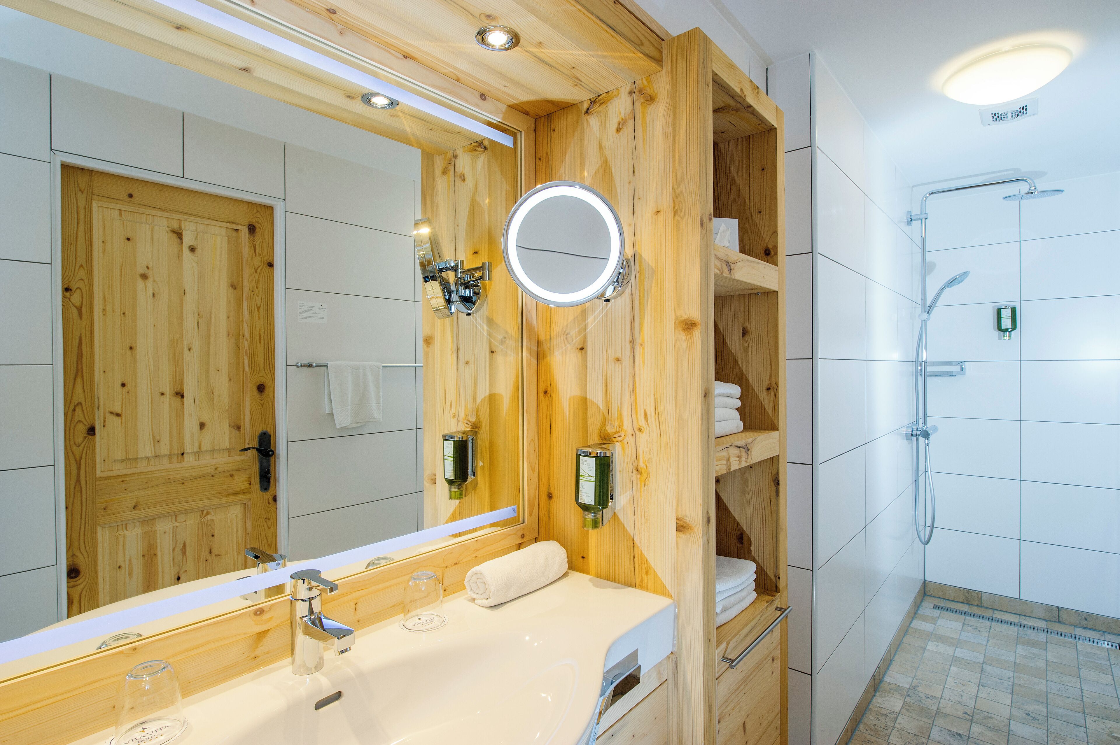 A wooden bathroom with a large mirror, a sink, and a shower.