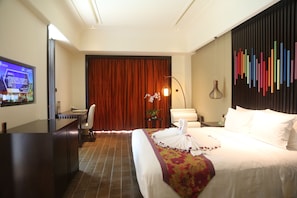 A hotel room with a bed, a desk, a chair, a television, and a wall with colorful vertical elements.