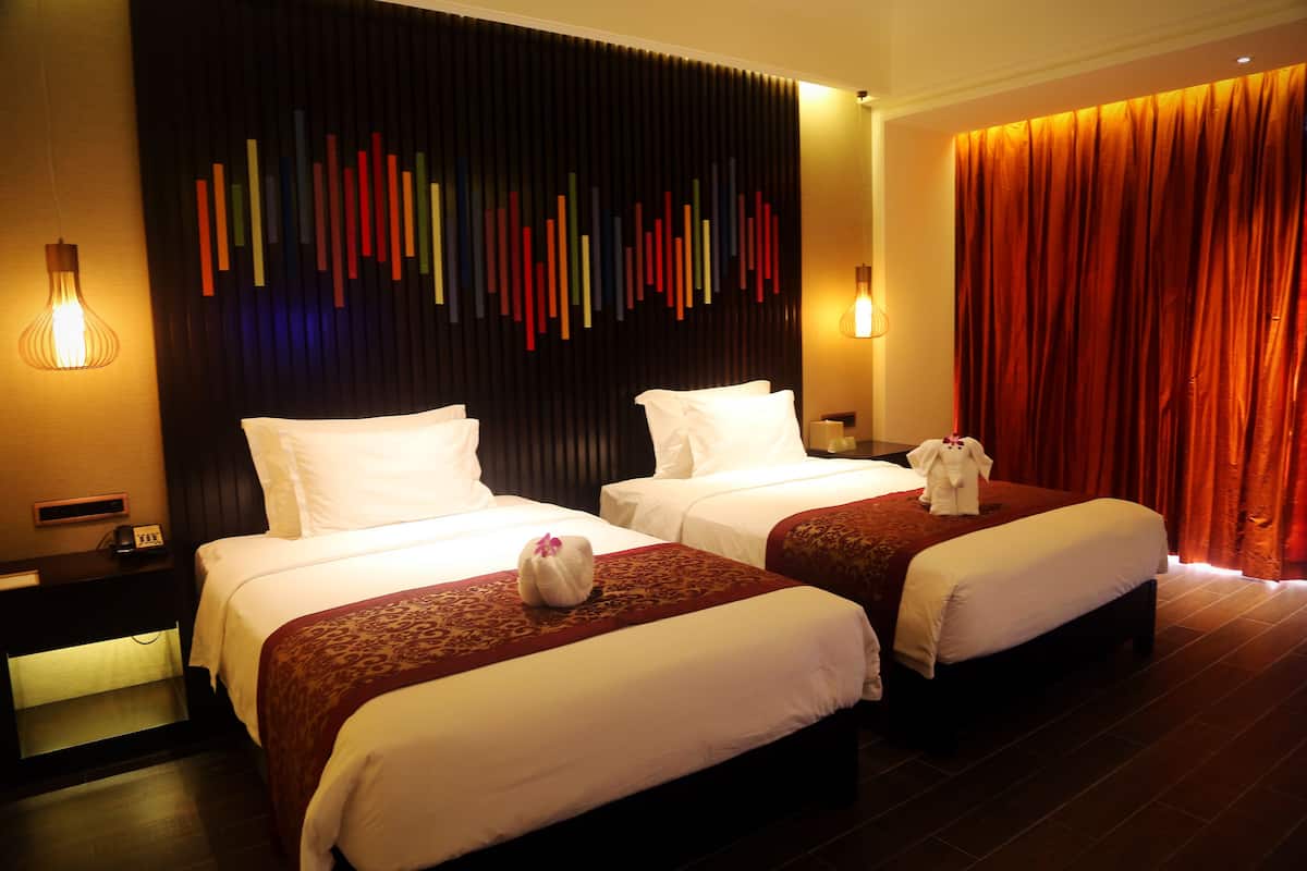 Une chambre d’hôtel avec deux lits, un mur sombre agrémenté d’éléments verticaux colorés et un rideau rouge.