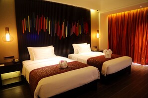 Ein Hotelzimmer mit zwei Betten, einer dunkel gestrichenen Wand mit farbigen vertikalen Elementen und einem roten Vorhang.