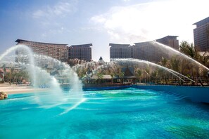 Ein großer Außenpool mit Wasserstrahlen, umgeben von Hochhäusern und Palmen.