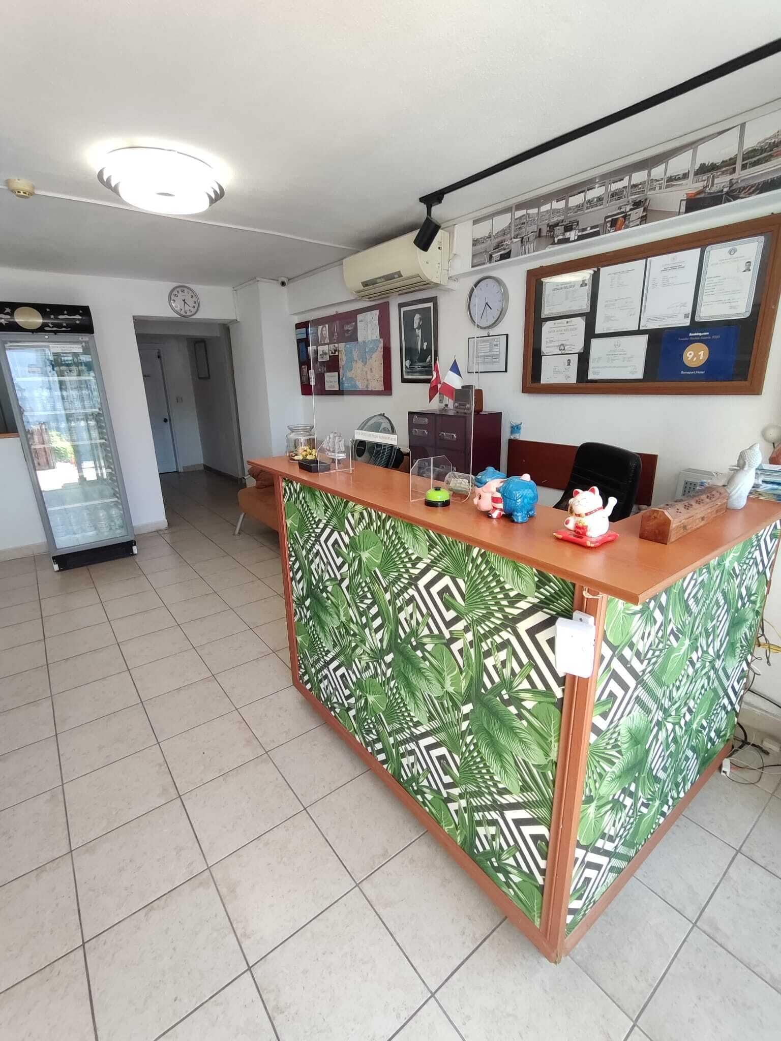 A reception desk with a green patterned backdrop, a clock, and a bulletin board with various notices.