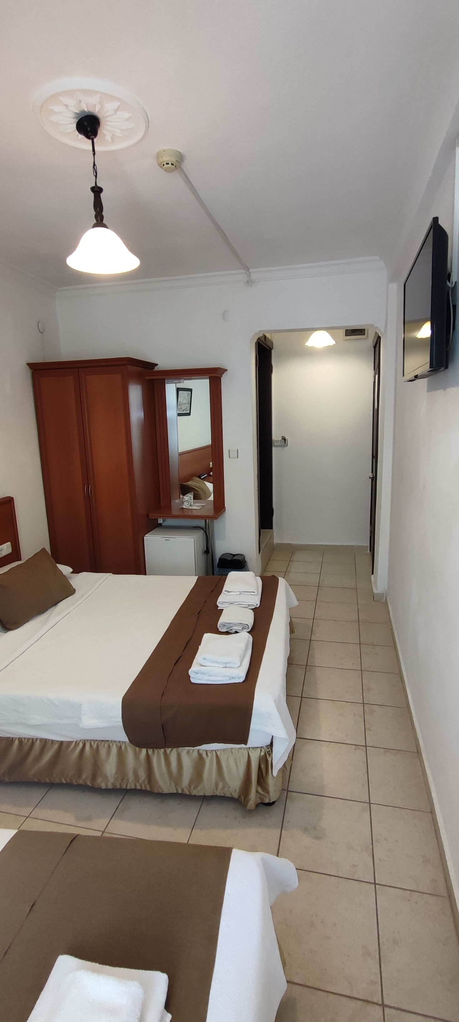 A hotel room with a bed, a desk, a wardrobe, and a bathroom visible through an open door.