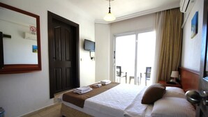 A hotel room with a bed, a TV, a door, and a view of the outside.