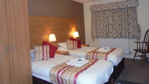 Ein Hotelzimmer mit zwei Betten, einem Holzkopfstück, Nachttischlampen, blumigen Vorhängen und einem Holzstuhl.