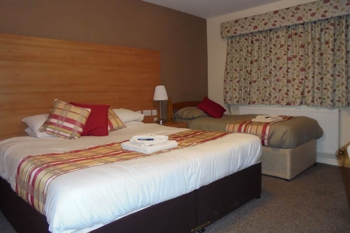 Una camera d'hotel con due letti, una testiera in legno, una finestra con tende floreali e una lampada sul comodino.