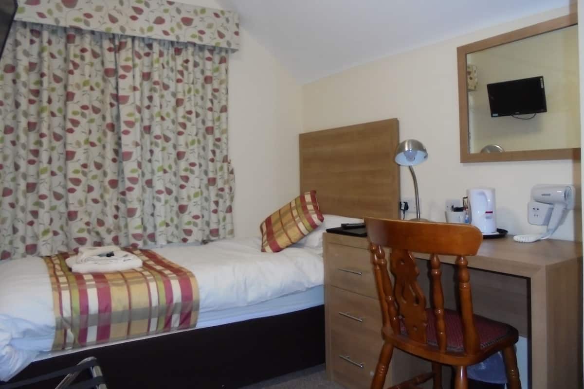 Una camera d'albergo con un letto, una scrivania con una sedia, una lampada, uno specchio e una televisione a parete.