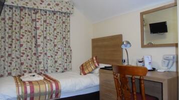 Habitación de hotel con cama, escritorio con silla, lámpara, espejo y televisión en la pared.