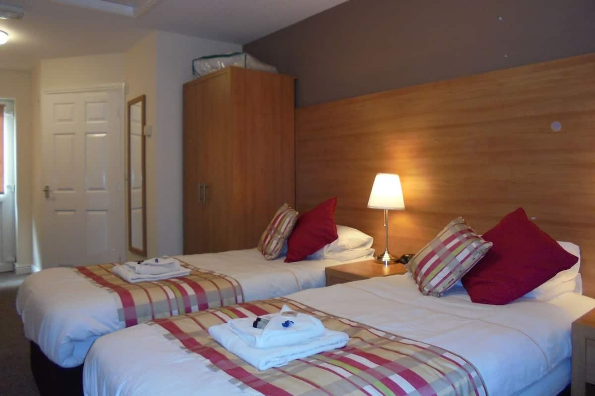 Camera d'albergo con due letti, una testiera in legno, un comodino con una lampada e un armadio.
