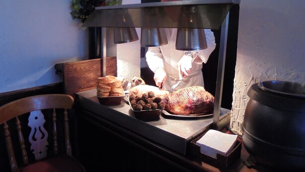 Ein Koch bereitet Essen hinter der Theke zu, wo Gebäck und ein Braten ausgestellt sind.