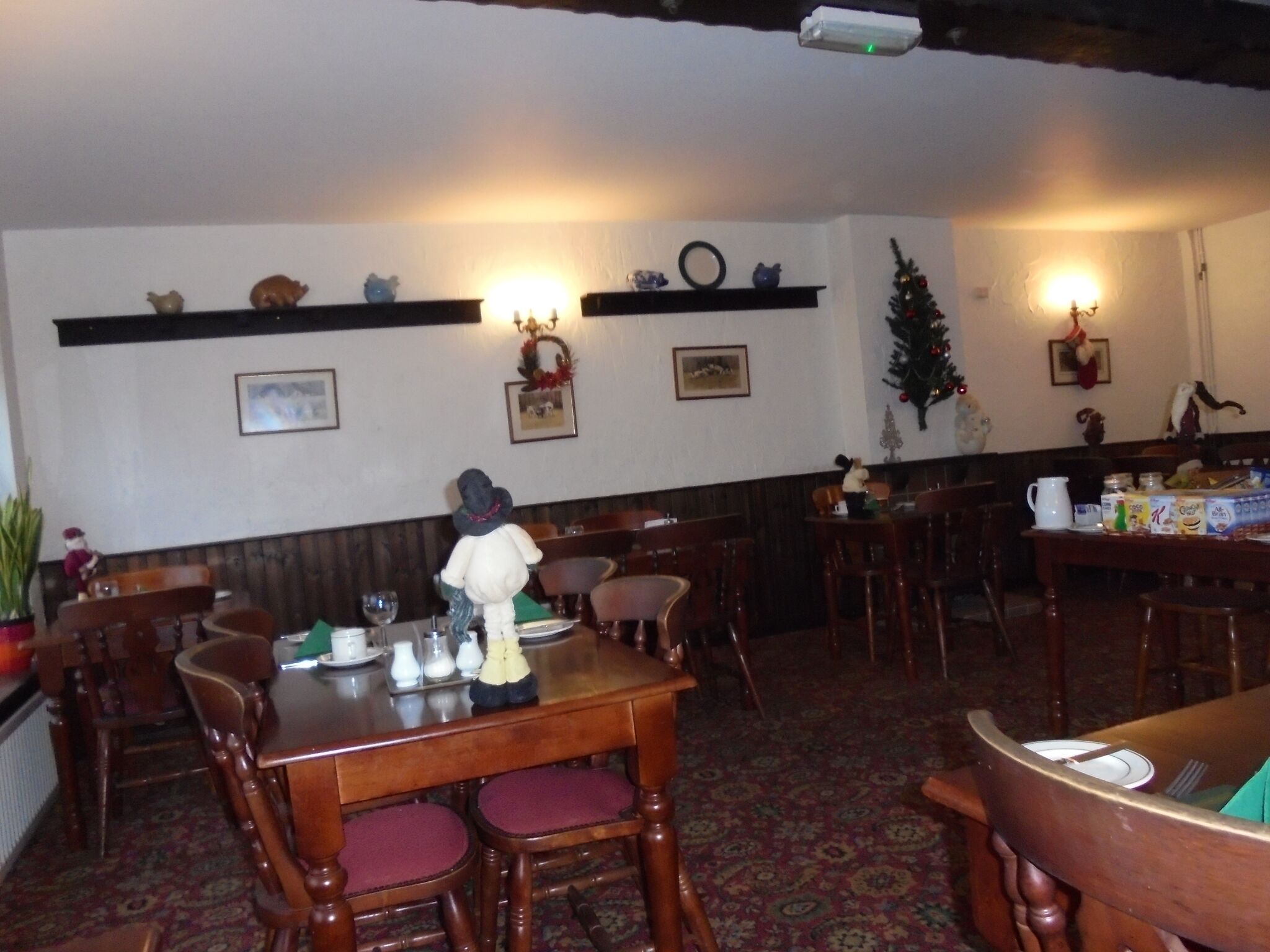 Un espace repas avec des tables et des chaises en bois, un sapin de Noël et des décorations fixées au mur.