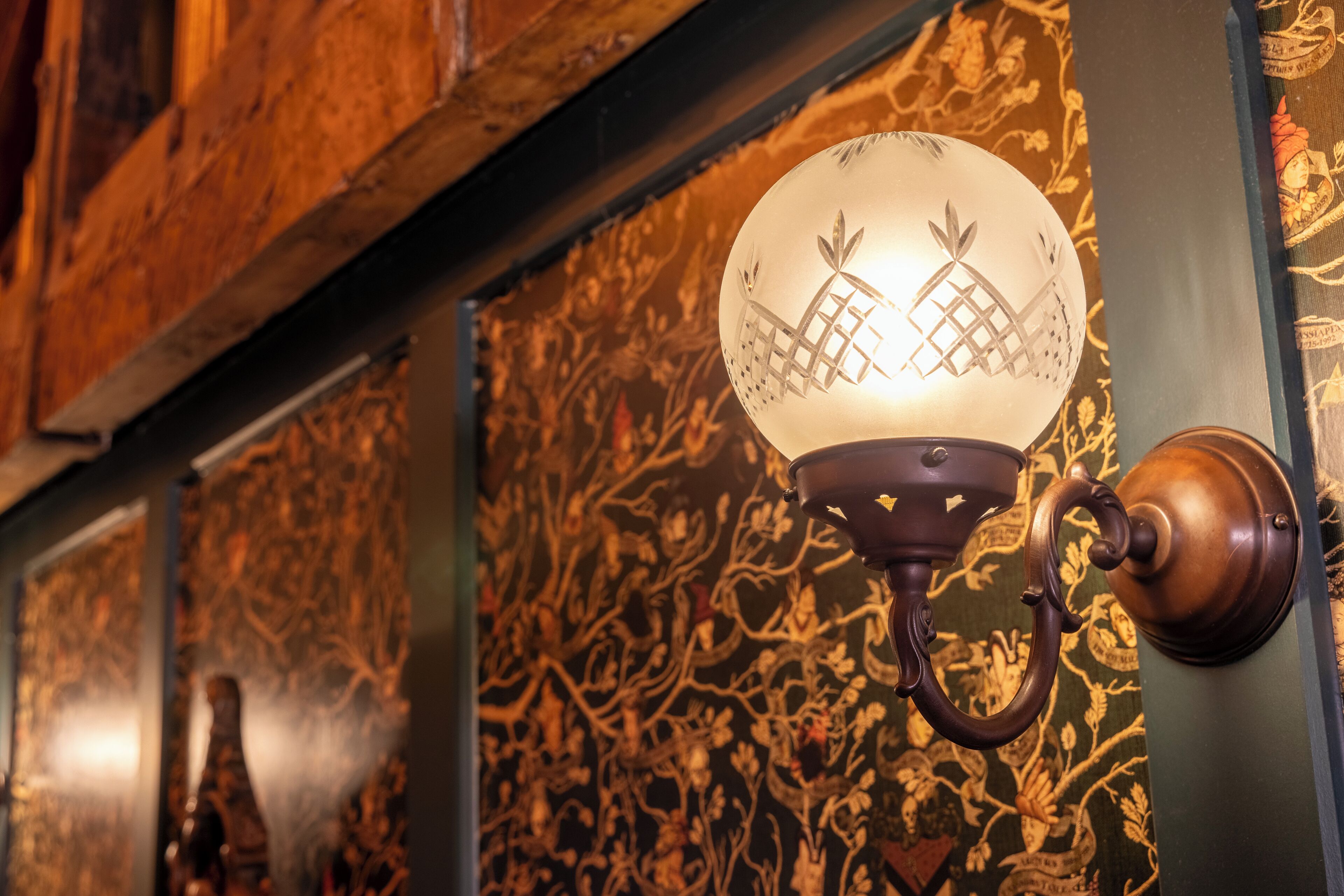 A wall-mounted light fixture with a decorative design, a wooden beam, and patterned wallpaper.