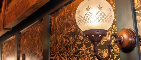 A wall-mounted light fixture with a decorative design, a wooden beam, and patterned wallpaper.