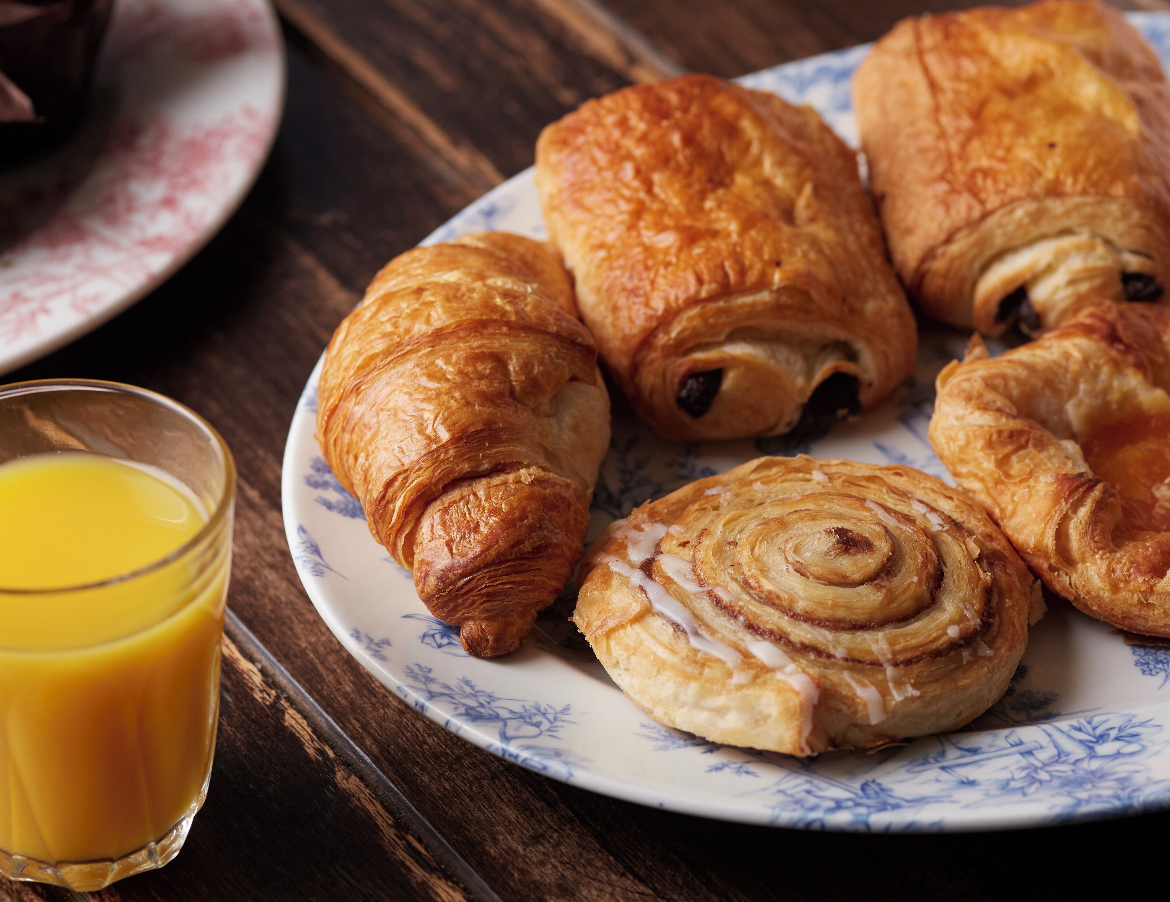 A plate of croissants and a glass of orange juice on a wooden table.