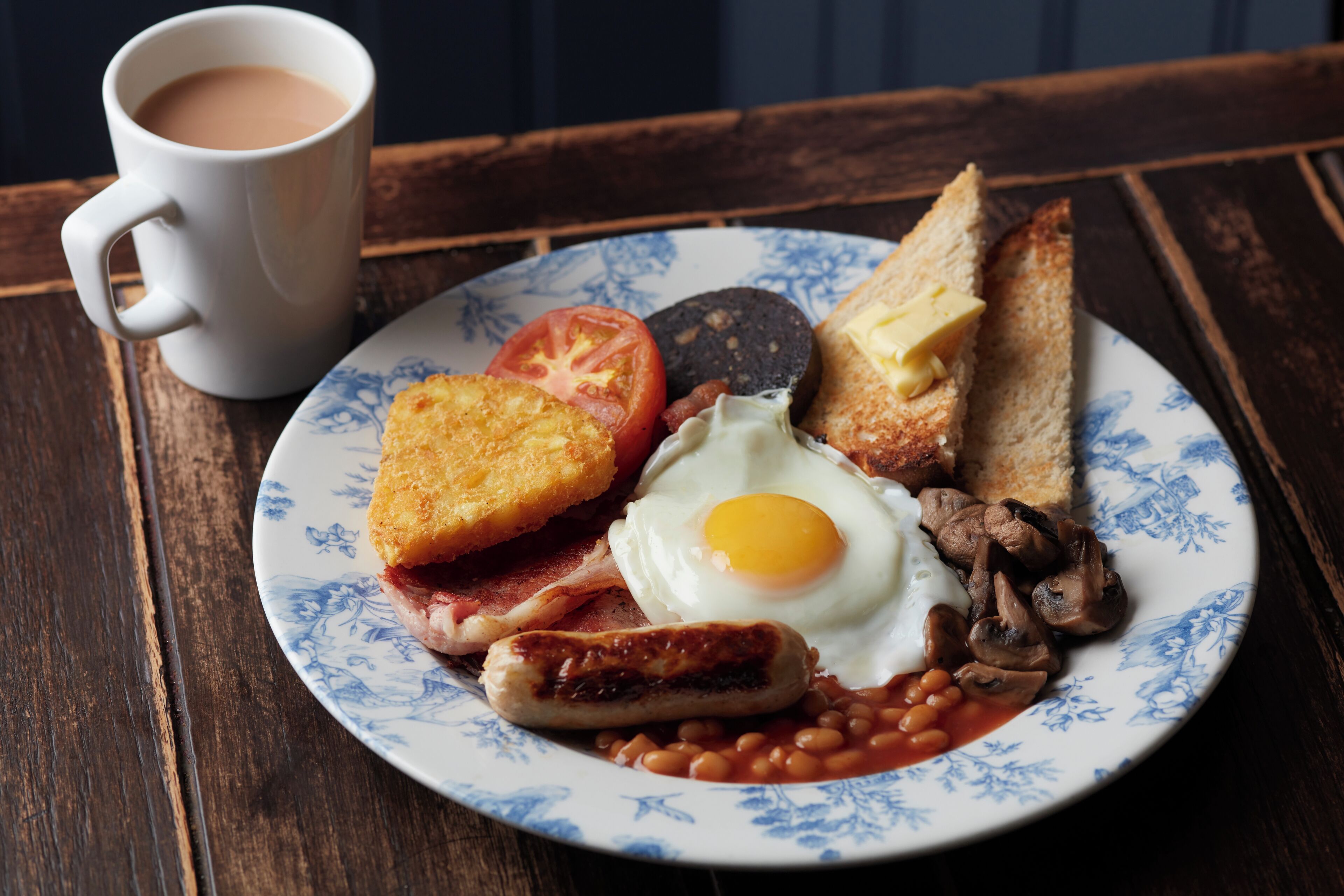 A plate of breakfast with toast, eggs, bacon, mushrooms, beans, and a sausage.