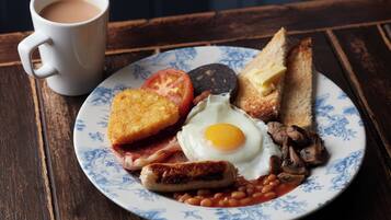 A plate of breakfast with toast, eggs, bacon, mushrooms, beans, and a sausage.