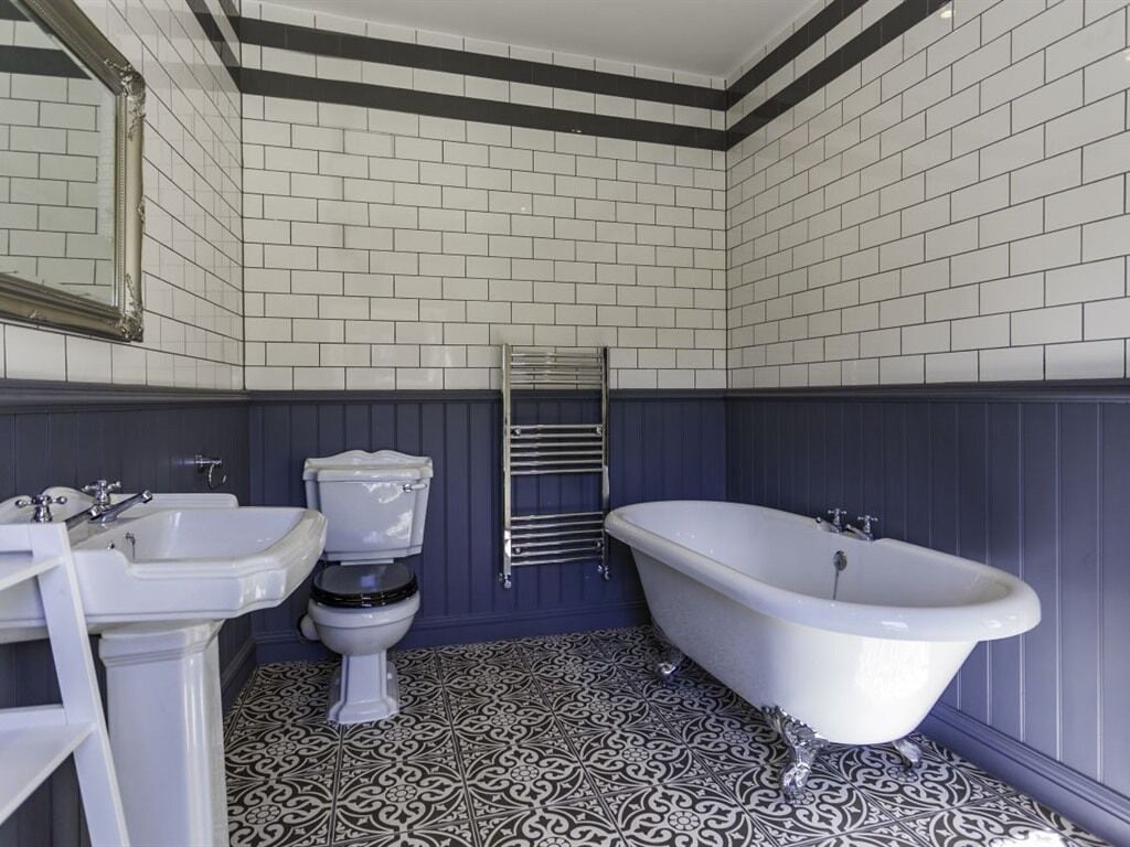 Een badkamer met een wit wastafelmeubel, toilet en bad, met vloertegels met een patroon en donkere wandbekleding.
