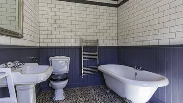 Een badkamer met een wit wastafelmeubel, toilet en bad, met vloertegels met een patroon en donkere wandbekleding.